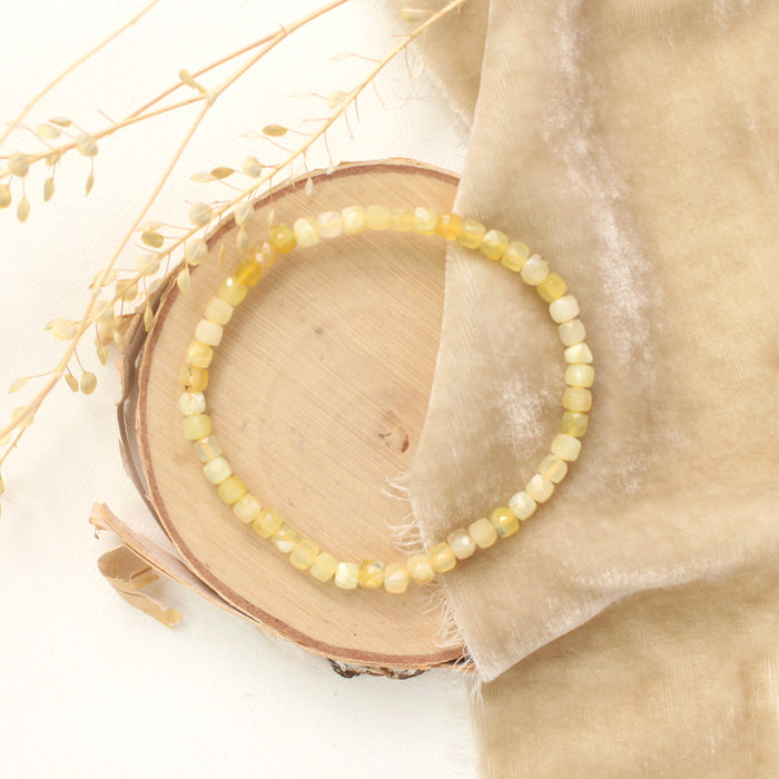 The yellow opal stretch bracelet styled on wood with tan velvet and dried grass
