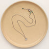 The zuni cross necklace styled on a tan plate to show the adjustable lobster clasp closure
