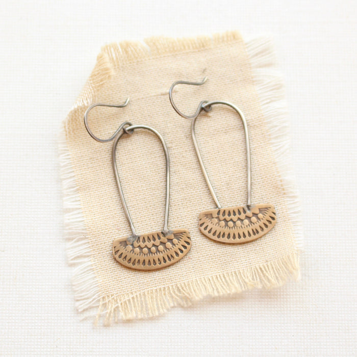 The stamped bronze and silver long loop asmi earrings styled on tan linen