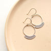 Stamped silver Asmi thin blade hoop earrings styled on a tan plate