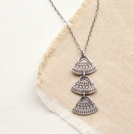 Stamped silver Asmi trio triangle necklace styled on tan linen
