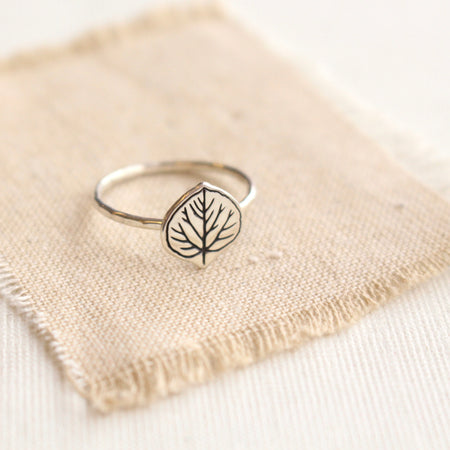 Stamped silver aspen leaf ring styled on tan linen