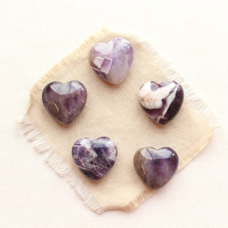 Five amethyst stone hearts styled on tan linen.