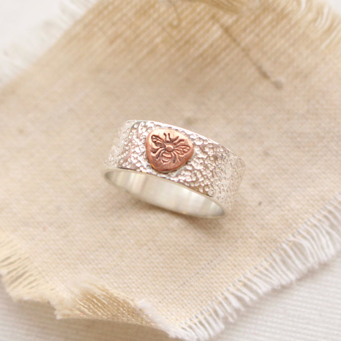 Sterling silver ring with copper bee on tan linen.