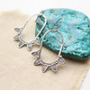 The tribal inspired feathered hoop earrings styled on tan linen with a blue stone