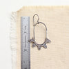 A feathered hoop earring next to a ruler for size reference