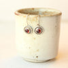 Garnet lobe hugger earrings perched on the edge of a small tan ceramic teacup.
