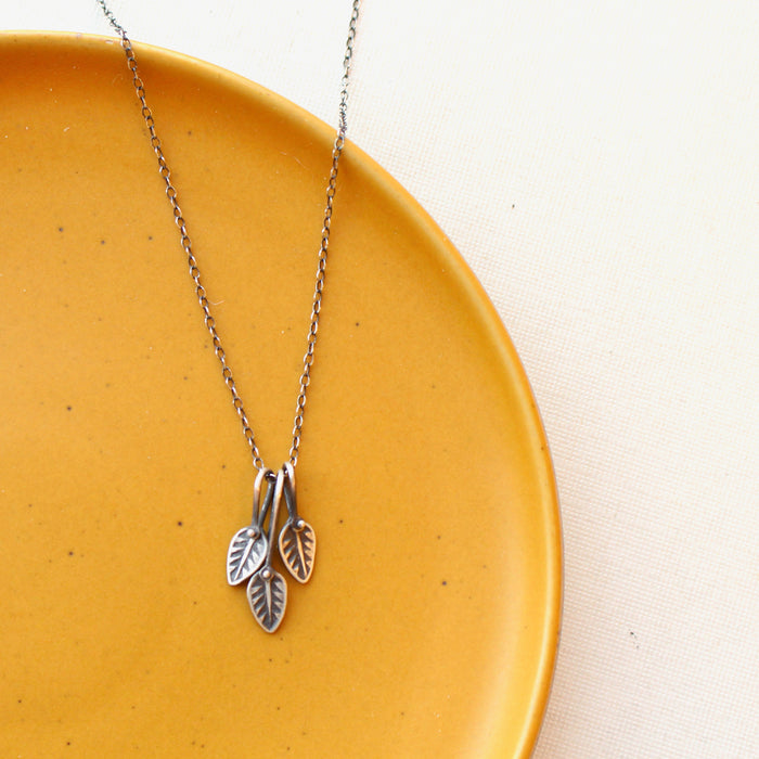 The stamped leaf trio necklace styled on a yellow plate