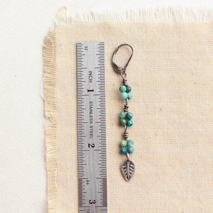 A stamped silver leaf and chrysocolla long earring next to a ruler for size reference