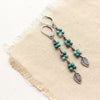 The stamped silver leaves and chrysocolla long earrings styled on tan linen