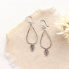 The stamped leaf teardrop hoop earrings styled on tan linen with a dried flower