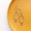 The forged silver leaf teardrop hoop earrings styled on a yellow plate
