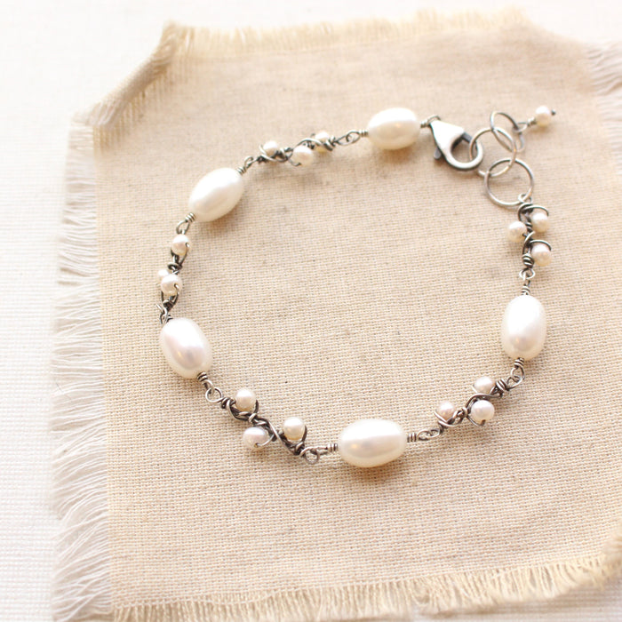 The wrapped pearl bud vine bracelet in silver styled on tan linen