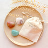3 heart shaped stones with drawstring linen bag styled on tan plate with dried leaves.