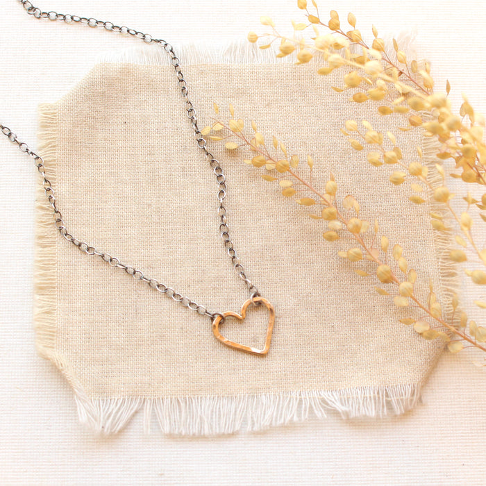 The mixed metal floating heart necklace styled on tan linen with dried grass