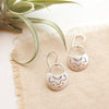 The stamped silver lotus half moon earrings styled on tan linen with an airplant