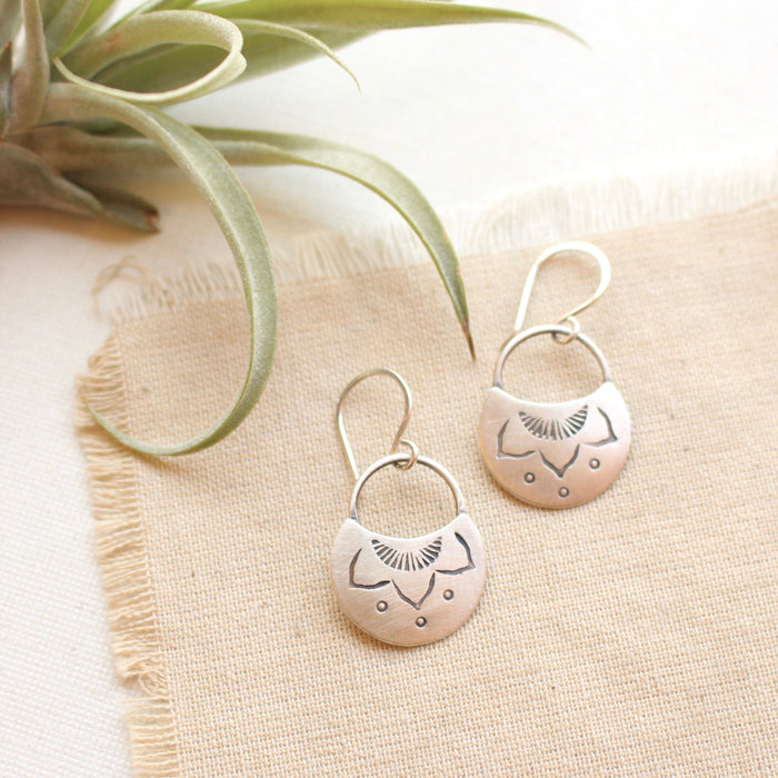 The stamped silver lotus half moon earrings styled on tan linen with an airplant