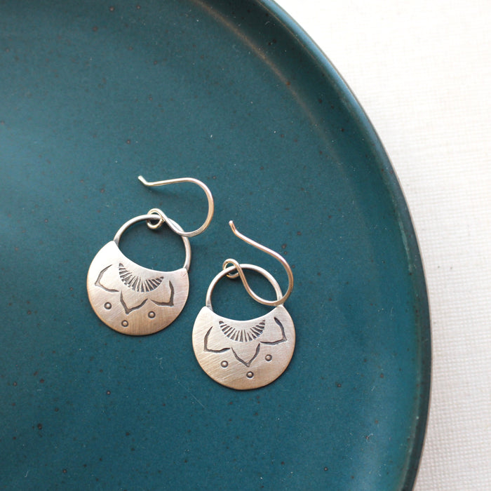 The stamped silver lotus half moon earrings styled on a blue plate