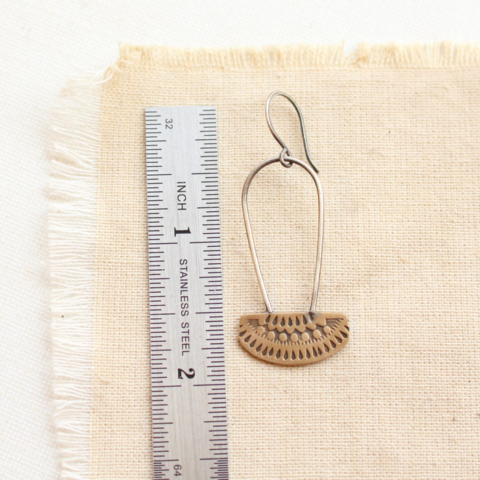 A stamped bronze and silver long loop asmi earring next to a ruler for size reference