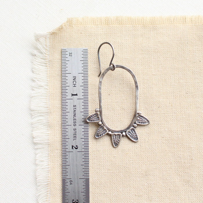 A feathered hoop earring next to a ruler for size reference