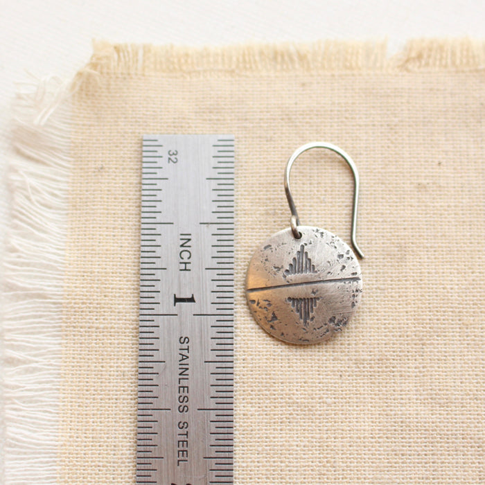 A pakal silver coin earring next to a ruler for size reference