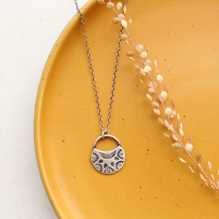 The midnight bloom necklace styled on a yellow plate with dried grass