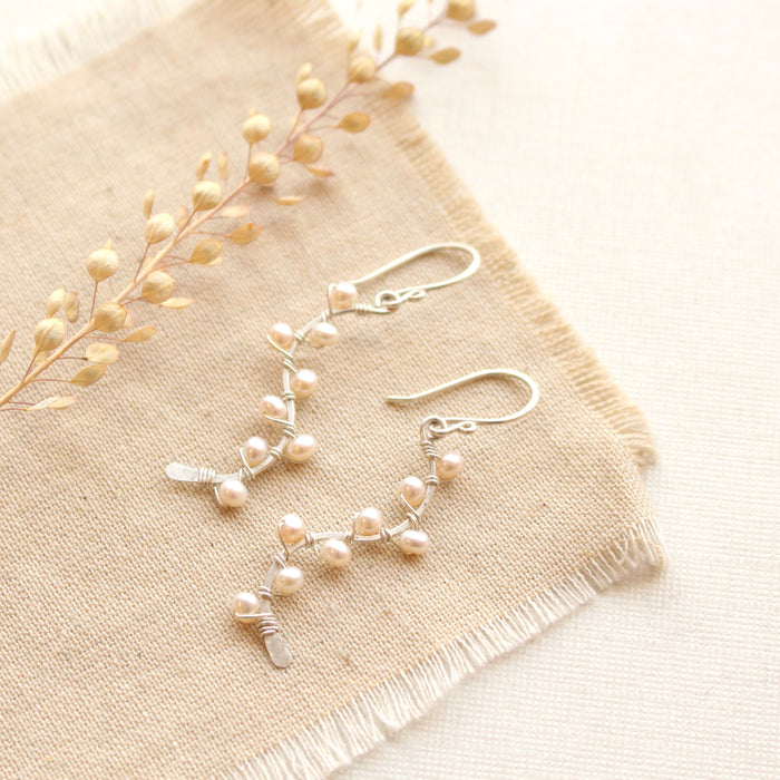 The elegant pearl wrapped silver vine earrings styled on tan linen with dried grass