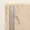 A pearl wrapped silver vine earring next to a ruler for size reference