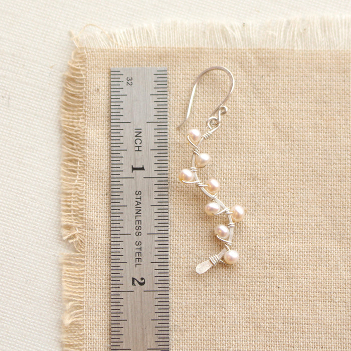 A pearl wrapped silver vine earring next to a ruler for size reference