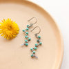 The southwest inspired turquoise wrapped silver vine earrings styled on a tan plate