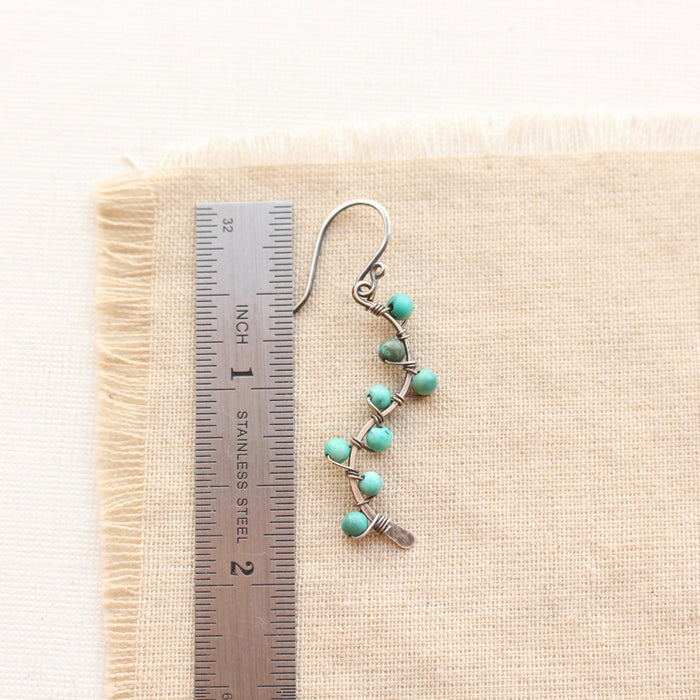 A turquoise wrapped silver vine earring next to a ruler for size reference