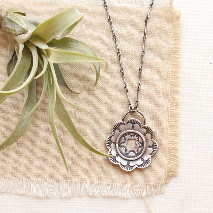 The columbine flower inspired stamped silver necklace styled on tan linen with an airplant