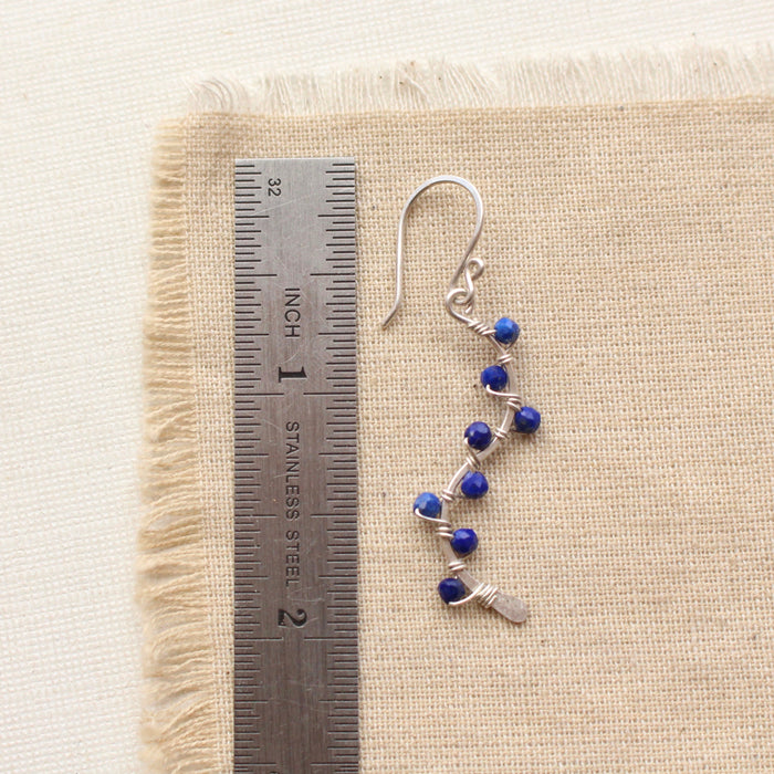 A lapis wrapped silver vine earring next to a ruler for size reference