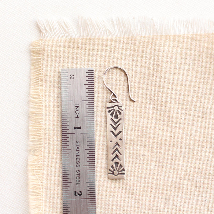 A sun bar earring next to a ruler for size reference