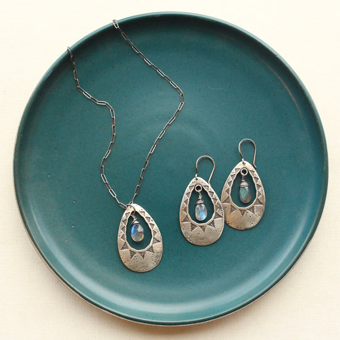 The pakal teardrop cutout labradorite long necklace styled with the matching earrings on a blue plate