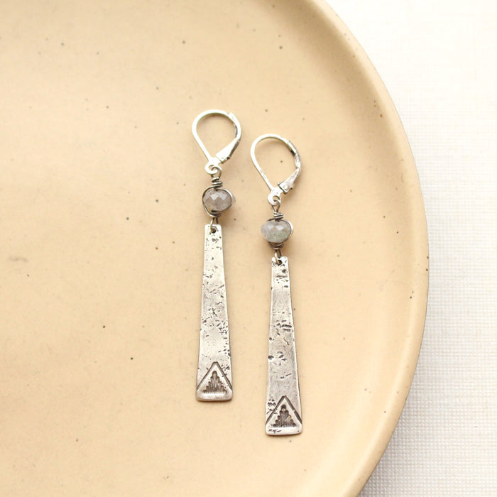 The pakal long triangle & labradorite earrings styled on a tan plate