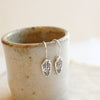 The rustic stamped silver feather lobe huggers styled on a ceramic cup