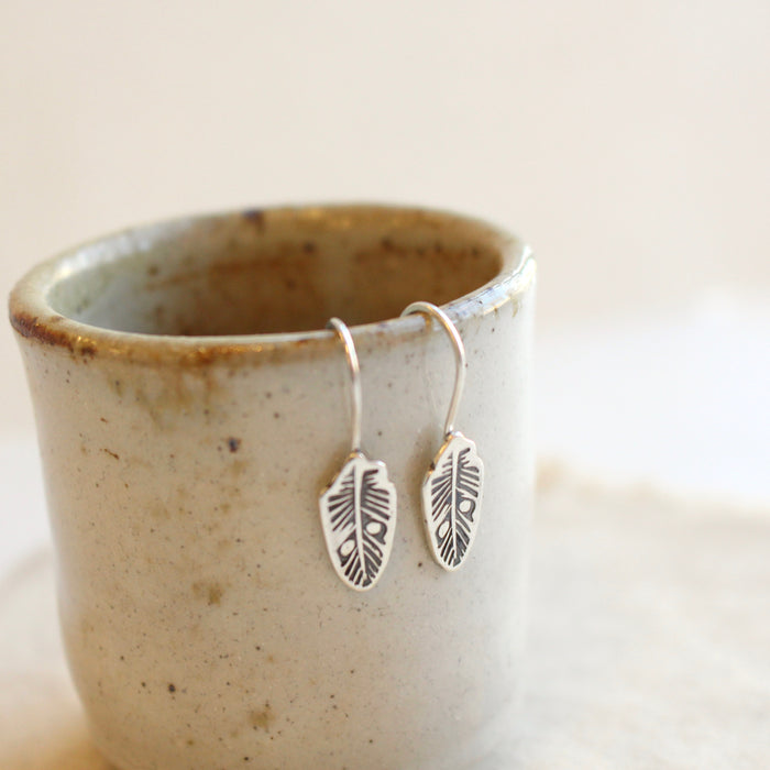 The rustic stamped silver feather lobe huggers styled on a ceramic cup