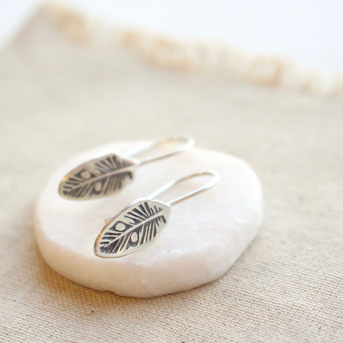 The southwest feather lobe hugger earrings styled on tan linen and a white rock