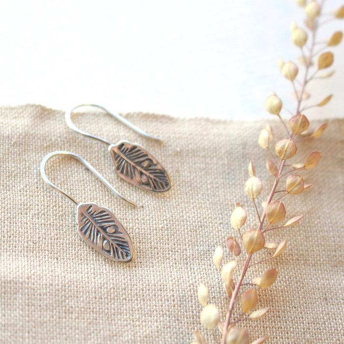 The bohemian feather lobe hugger earring styled on tan linen with dried grass