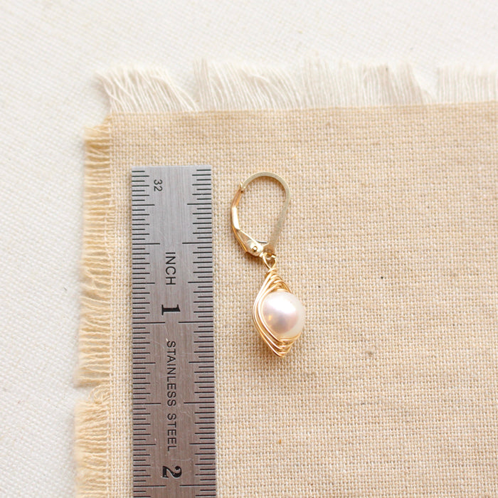 A perfect pearl gold wrapped earring next to a ruler for size reference
