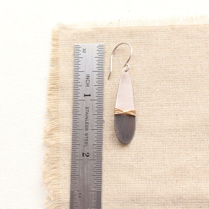 A dipped teardrop mixed metal earring next to a ruler for size reference