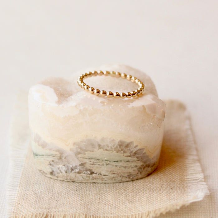 14k gold fill beaded stacking ring styled on a white crystal and tan linen