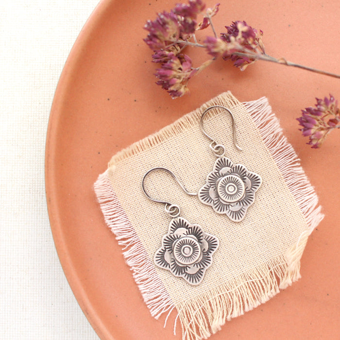 The talara winter sun earrings styled on a red plate with linen and a dried flower