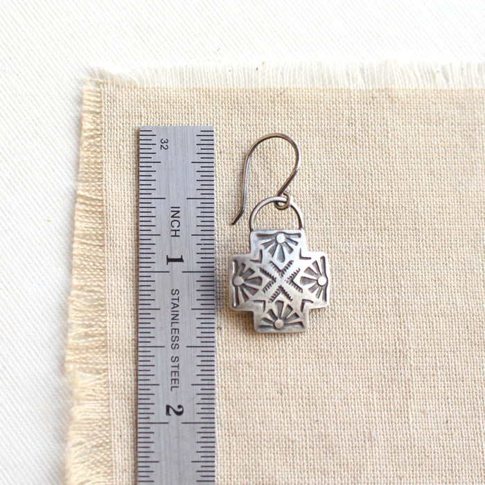 A sun cross earring next to a ruler for size reference