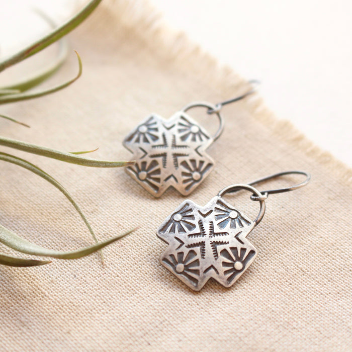 The southwest stamped silver sun cross earrings styled on tan linen with an airplant