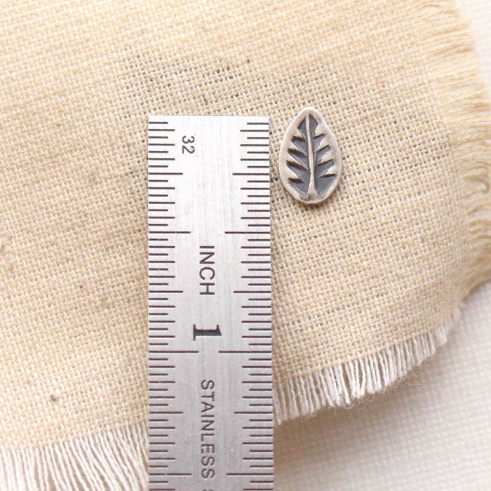 A stamped silver leaf post earring next to a ruler for size reference
