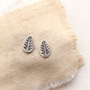 The stamped silver leaf post earrings styled on tan linen