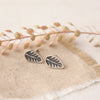 The stamped silver leaf post earrings styled on tan linen with dried grass