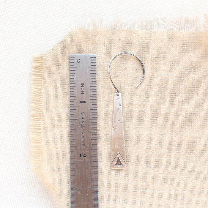A pakal long triangle hoop earring next to a ruler for size reference